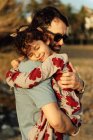 Seitenansicht eines erwachsenen Mannes mit Sonnenbrille, der am Wochenende auf dem Land Mädchen mit geschlossenen Augen trägt und umarmt — Stockfoto