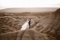 Alto angolo di sposo e sposa che si abbracciano vicino alla montagna contro il cielo nuvoloso al tramonto nel Parco Naturale di Bardenas Reales in Navarra, Spagna — Foto stock