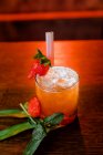Высокий угол коктейля Сан-Франциско из водки и апельсинового сока, украшенного клубникой и кубиками льда на пальмовых листьях — стоковое фото