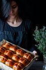 Female baker holding puff freshly baked hot cross buns on baking tray — Stock Photo