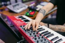Crop невідомий татуйований піаніст, який грає сучасний синтезатор, створюючи музику за столом у студії звукозапису — стокове фото