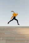 Young athletic caucasian woman wearing headphones and sport outfit, jumping on stairs outdoors — Stock Photo
