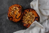 Dall'alto di metà di zucca al forno sane appetitose saporite con semi su tavolo grigio con stoffa da cucina — Foto stock