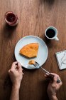 Top view of anonymous person taking piece of fresh pumpkin pie with fork from plate over lumber table with jam and hot beverage — Stock Photo