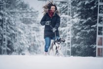 Cão caçador doméstico bonito correndo com mulher entre árvores na floresta de inverno — Fotografia de Stock