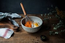 Whisk utensílio em uma tigela com purê de abóbora, ovos e farinha para preparação de torta na mesa de madeira perto de tábua de corte e toalha — Fotografia de Stock