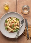 From above dish of pasta with arugula, salami and walnuts on a table surrounded by oil, lemon and cutlery — Stock Photo