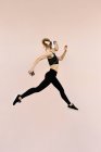 Jovem mulher branca atlética usando fones de ouvido e roupas esportivas, pulando contra fundo brilhante ao ar livre — Fotografia de Stock