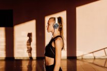 Молода атлетична біла жінка слухає музику із закритими очима та розслабляється на заході сонця, тіні та світло на фоні — стокове фото