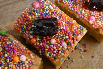 From above of sweet Turron de Dona Pepa cakes with nougat decorated with colorful dragee and prunes served on wooden table — Stock Photo