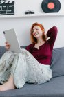 Contenuto giovane donna seduta sul divano mentre parla con il partner durante la videochat sul tablet in casa — Foto stock