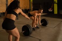 Fit male athlete doing deadlift exercise with barbell under supervision of female personal trainer during workout in gym — Stock Photo