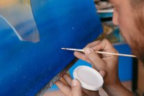 Cortado homem barbudo irreconhecível pintando pontos com pigmento branco sobre tela com imagem abstrata durante o trabalho em oficina criativa — Fotografia de Stock