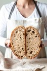 Crop manos de mujer sin rostro sosteniendo pan de centeno masa fermentada recién horneada miga de corte blanco por la mitad - foto de stock