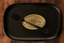 Top view of black fork placed near sealed canned food on rectangular black tray — Stock Photo