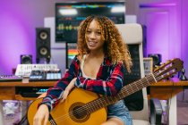 Young African American female guitarist with classical guitar sitting in studio while looking at camera — Stock Photo