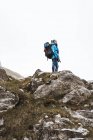 Vista lateral da mulher tranquila em casaco azul brilhante com mochila em pé na colina rochosa e olhando para longe — Fotografia de Stock