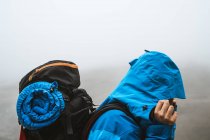 Vista lateral da mulher tranquila irreconhecível em casaco azul brilhante andando com mochila olhando para baixo no vale seco em neblina nebulosa — Fotografia de Stock