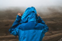 Visão traseira da mulher tranquila irreconhecível em casaco azul brilhante em pé na colina rochosa — Fotografia de Stock