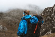 Visão traseira da mulher tranquila em casaco azul brilhante com mochila em pé na colina rochosa e olhando para longe — Fotografia de Stock