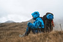 Вид збоку на невпізнавану спокійну жінку в яскраво-блакитній куртці, яка відпочиває з рюкзаком, насолоджуючись видами, дивлячись у суху долину в туманному тумані — стокове фото