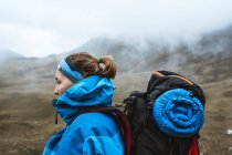 Seitenansicht einer ruhigen anonymen Frau in hellblauer Jacke mit Rucksack, die auf einem felsigen Hügel steht und wegschaut — Stockfoto