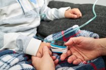 Crop donna irriconoscibile utilizzando pulsossimetro moderno sul dito del bambino per misurare il livello di ossigeno nel sangue — Foto stock