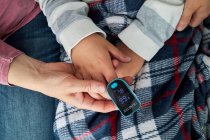 Draufsicht der Ernte unkenntlich Frau mit modernen Pulsoximeter am Finger des Kindes zur Messung des Sauerstoffspiegels im Blut — Stockfoto