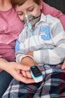 Crop donna irriconoscibile utilizzando pulsossimetro moderno sul dito del bambino per misurare il livello di ossigeno nel sangue — Foto stock