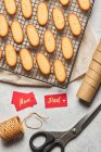 Dall'alto di gustosi biscotti natalizi disposti su rete metallica da forno sul tavolo con assortiti materiali da imballaggio — Foto stock