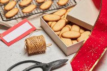 Сверху вкусное рождественское печенье, помещенное на металлическую сетку для выпечки и коробку на столе с разнообразными упаковочными материалами — стоковое фото