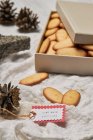 Alto ángulo de etiqueta de regalo y conos colocados en la mesa con caja llena de galletas dulces caseras de Navidad - foto de stock