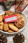 Von oben Teller mit verschiedenen süßen Keksen und Geschenkanhänger auf den Tisch mit Weihnachtsdekoration gestellt — Stockfoto