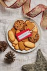 Von oben Teller mit verschiedenen süßen Keksen und Geschenkanhänger auf den Tisch mit Weihnachtsdekoration gestellt — Stockfoto