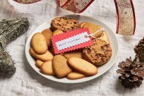 From above of plate with various sweet biscuits and gift tag placed on table with Christmas decorations — Stock Photo