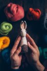 Mãos segurando um coelho de Páscoa feito à mão feito de lã e sentido na mesa de madeira escura — Fotografia de Stock