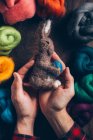 Hands holding a hand made easter rabbit made of wool and felt on dark wooden table — Stock Photo
