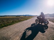Вид сбоку человек за рулем мотоцикла на сельской дороге при солнечном свете в сельской местности — стоковое фото