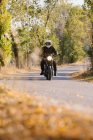Homem de jaqueta de couro e capacete andar de bicicleta na estrada de asfalto no dia ensolarado de outono no campo — Fotografia de Stock