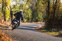Mann in Lederjacke und Helm fährt Fahrrad auf Asphaltstraße an sonnigem Herbsttag im Grünen — Stockfoto
