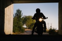 Силуэт неузнаваемого гонщика, сидящего на мотоцикле с включенными фарами в туннеле — стоковое фото