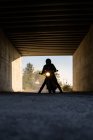 Silhouette of unrecognizable racer sitting on motorbike with switched on headlamps in tunnel — Stock Photo