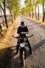 Concentrated aged male racer in leather jacket fastening helmet and sitting on motorbike in autumn sunny day — Stock Photo