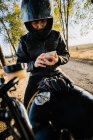 Concentrated male racer in leather jacket sitting on motorbike and browsing phone in autumn sunny day — Stock Photo
