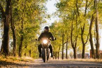 Homme en veste en cuir et casque à vélo sur route asphaltée en automne ensoleillé à la campagne — Photo de stock
