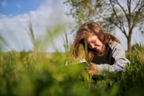 Encantada menina adolescente sentado no prado e desenho em caderno de esboços enquanto desfruta de dia ensolarado no campo — Fotografia de Stock