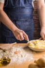 Невпізнаваний чоловік в фартусі додає картопляне пюре до борошна і сире яйце під час приготування тіста для ноккі на кухні — стокове фото