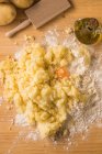 Top view of egg yolk placed in heap of mashed potatoes and wheat flour near oil and ribbed board during gnocchi preparation on table — Stock Photo
