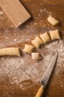 Top view of pieces of soft raw tough placed on wooden table covered with flour near ribber board and knife during gnocchi preparation in the kitchen — стоковое фото