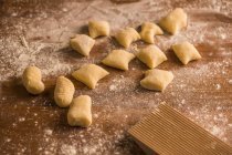 Top view of pieces of soft raw dough placed on wooden table covered with flour near ribber board during gnocchi preparation in the kitchen — Stock Photo